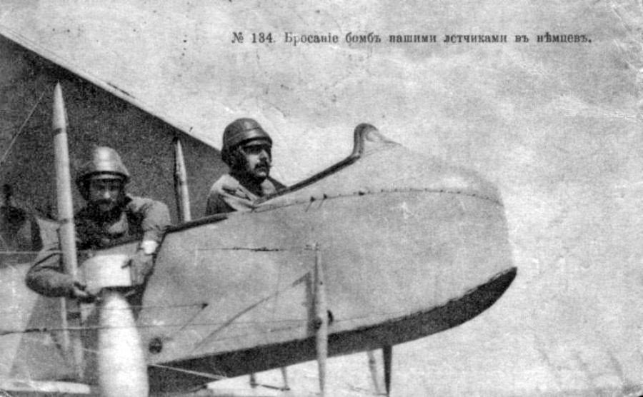 Открытка 1910-х годов: двое авиаторов в кожаных шлемах в открытой кабине, у наблюдателя в руках авиабомба